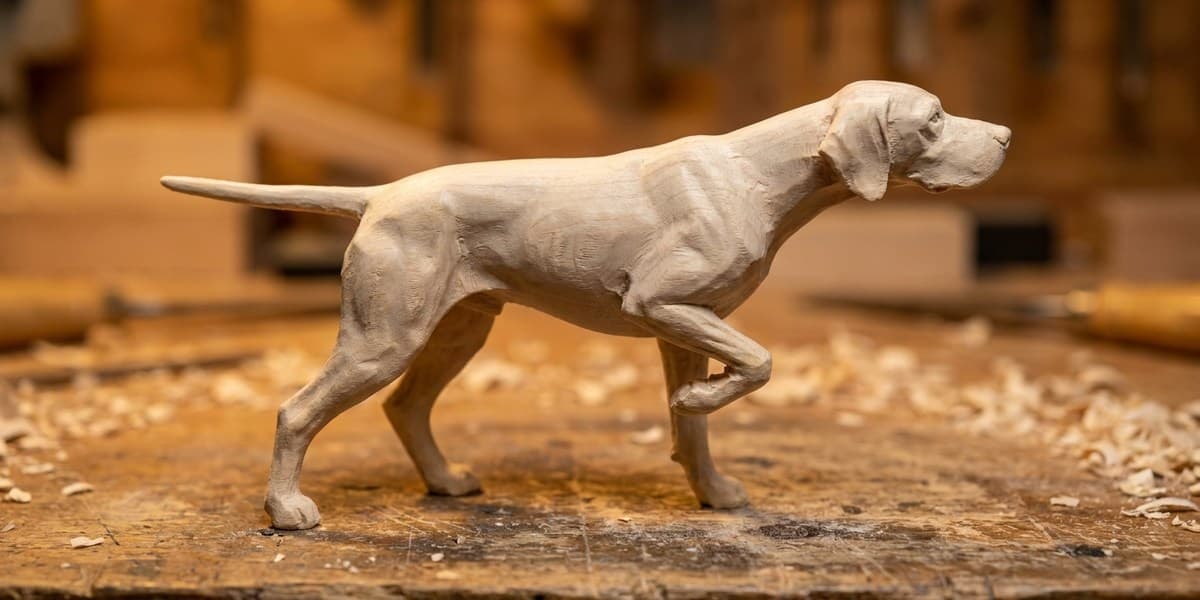English Pointer wood carving in progress — raw basswood mid-process stage showing the classic pointing pose before finishing and paint.